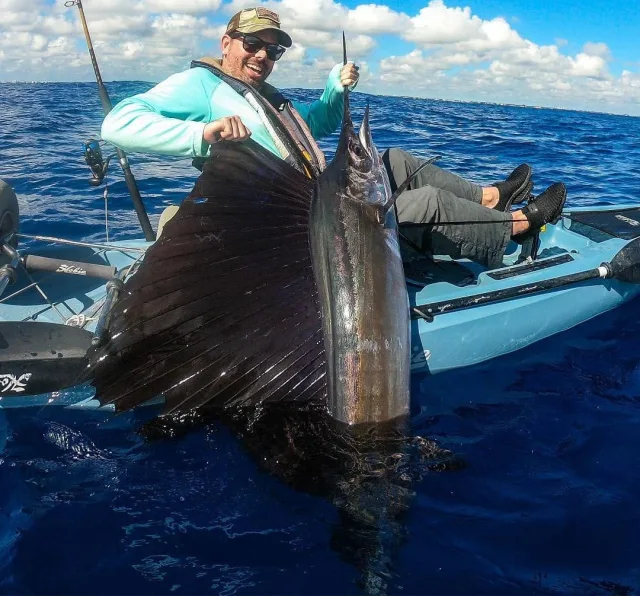Keith Caron on a kayak holding a sailfish, its sail fanned out, off the Florida coast
